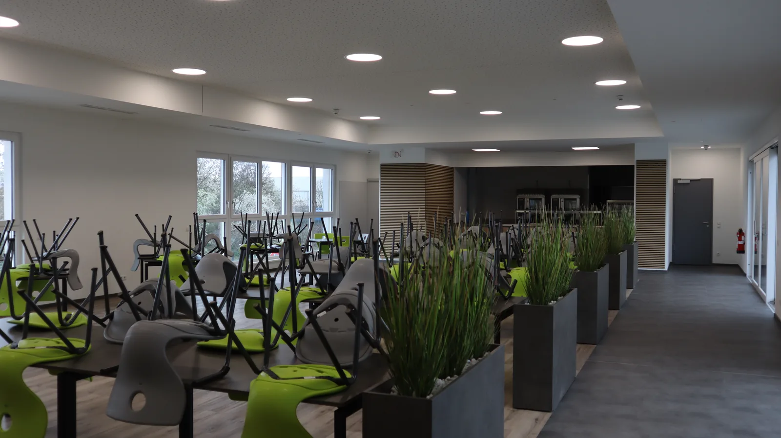 Cafeteria mit gestapelten Stühlen und Pflanzkübeln als Raumteiler